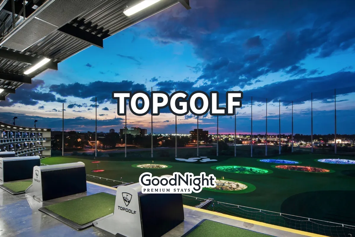 This lively evening exterior captures the bright, engaging atmosphere at Topgolf, with golf hitting bays illuminated against the twilight sky and colorful target areas inviting friendly competition. The mood is both exciting and relaxed, perfect for group gatherings.