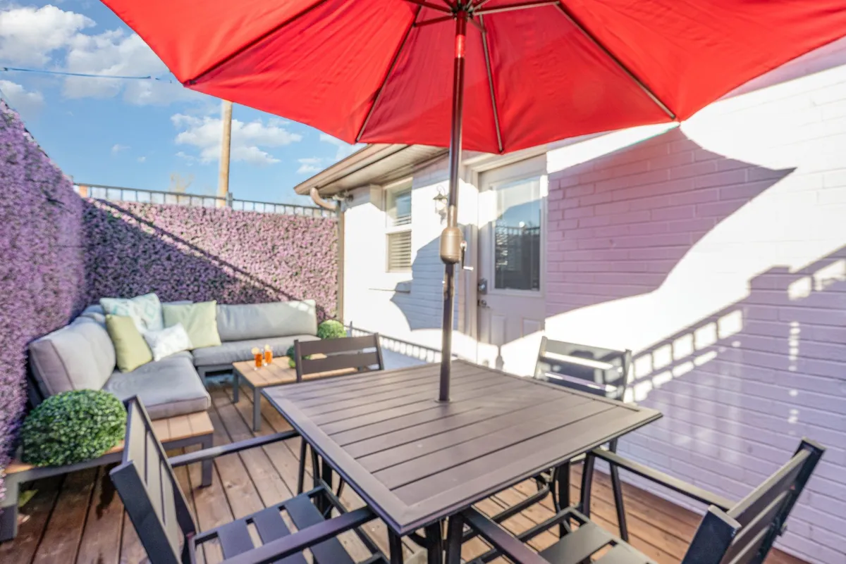 This image features a private patio with a red umbrella, comfortable outdoor lounge seating, a wooden deck, and decorative plants. The area is inviting and ideal for relaxing or socializing in a serene outdoor setting.