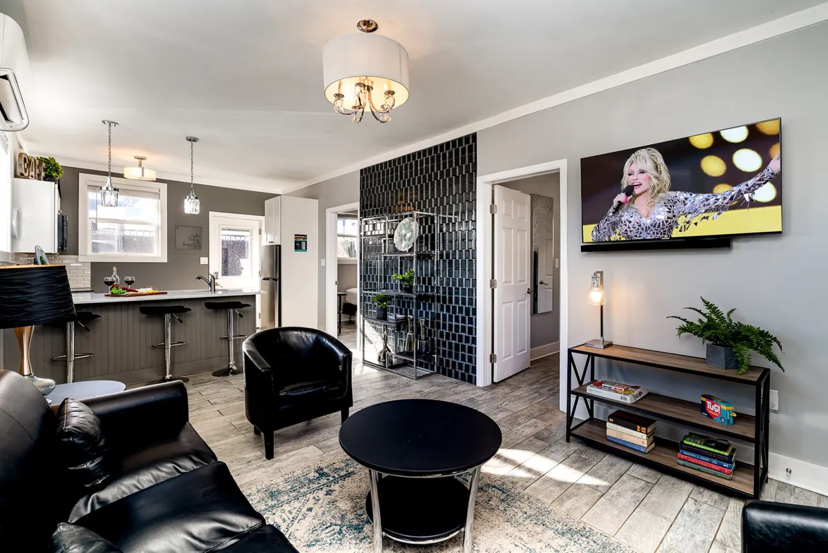 The image captures an inviting living area with a sleek black leather sofa, stylish round coffee table, contemporary black accent chairs, and a large TV set against a decorative wall. The space exudes a cozy yet lively atmosphere perfect for relaxing, socializing, or hosting gatherings with friends and family.