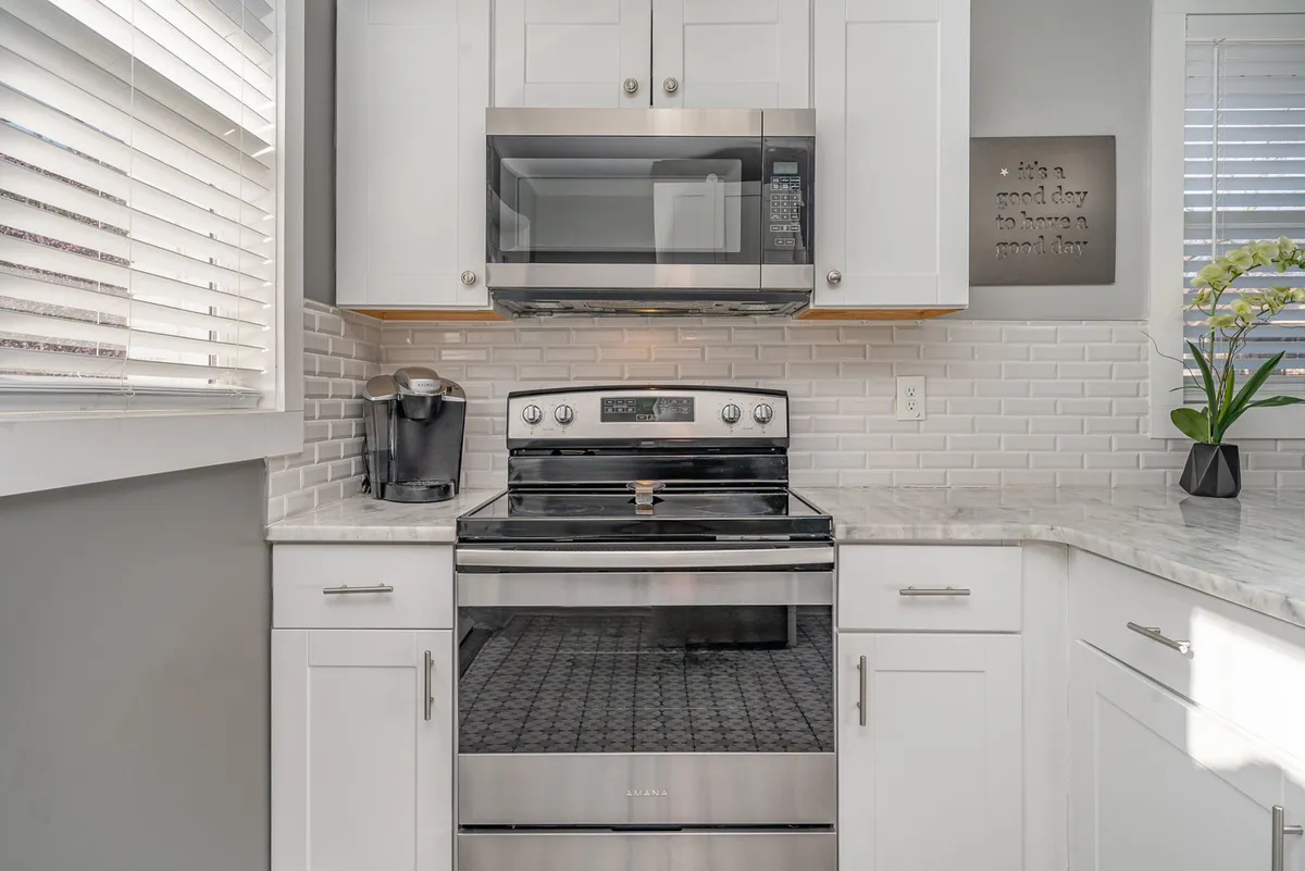 A cheerful, modern kitchen with marble countertops, stainless steel appliances, white cabinetry, and a decorative sign. The space is bright, functional, and tailored for preparing both quick breakfasts and celebratory dinners.
