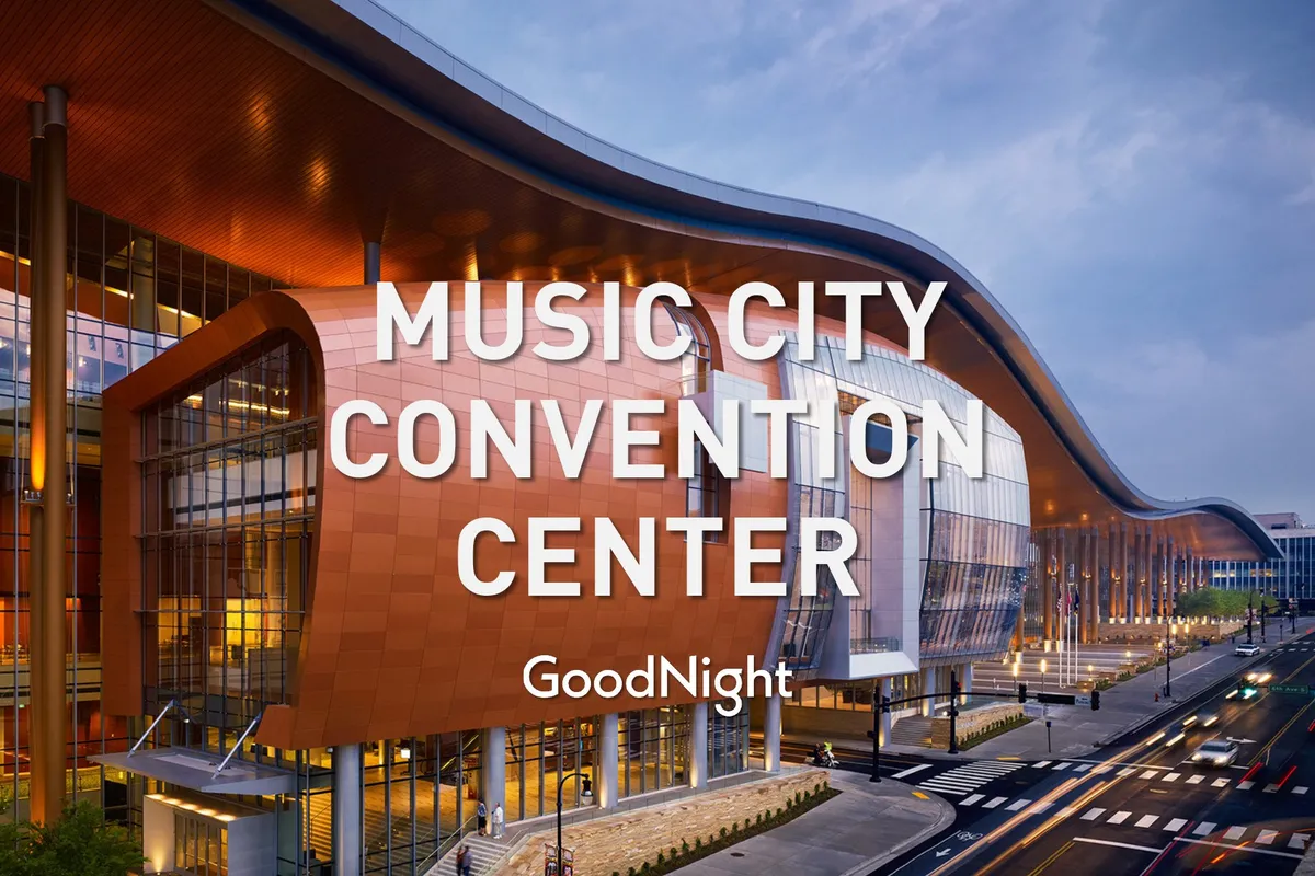 The image captures the striking exterior of a modern conference and event venue, with its curved roof structure, expansive glass windows, and an illuminated entryway. The architecture signals a hub for business gatherings, networking events, and major conferences within the city center.