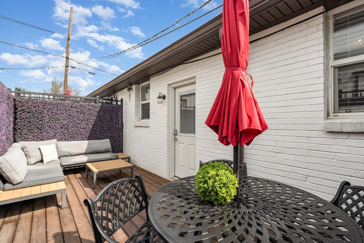 A private patio space with a bold red umbrella, comfortable outdoor seating, a decorative plant, and a relaxed ambiance, perfect for socializing or enjoying a nightcap after a night out.