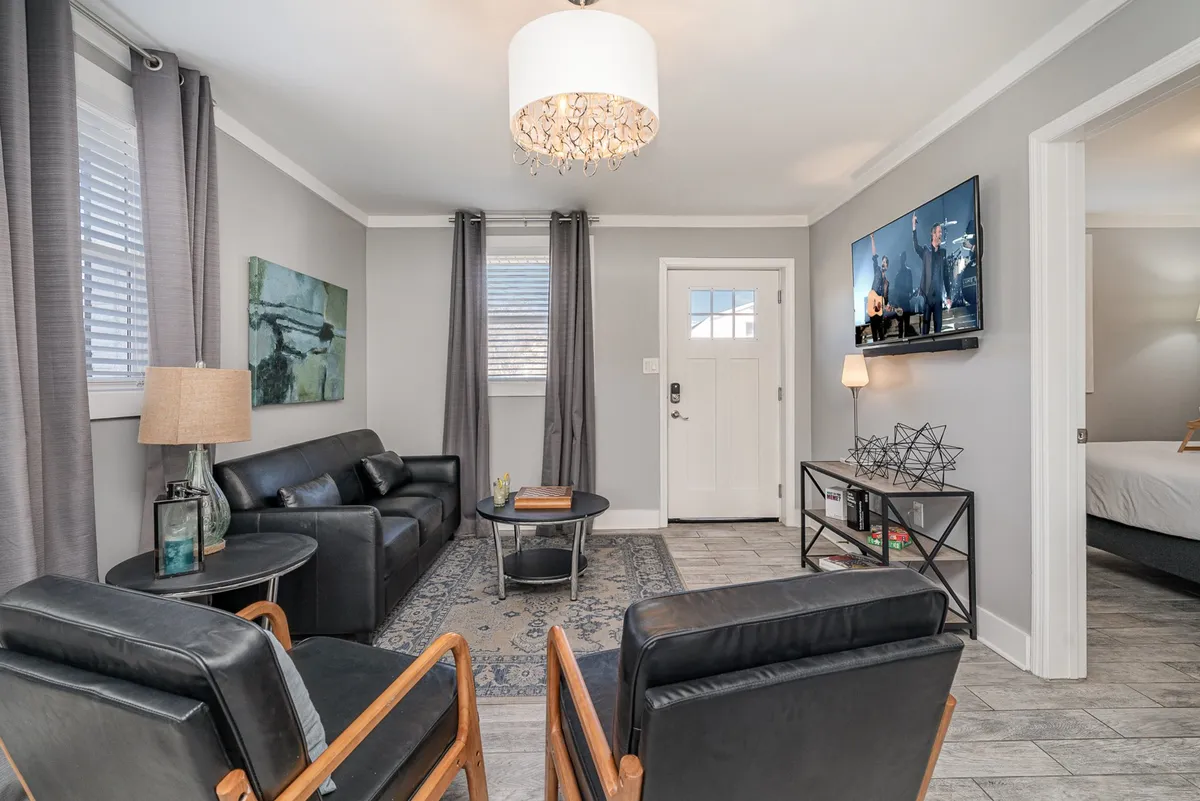 A comfortable living room with a plush sofa, armchairs, a coffee table, and a TV situated to one side. Soft ambient lighting and tasteful decor create a space that feels both intimate and welcoming, ideal for relaxation or gathering with friends and family.